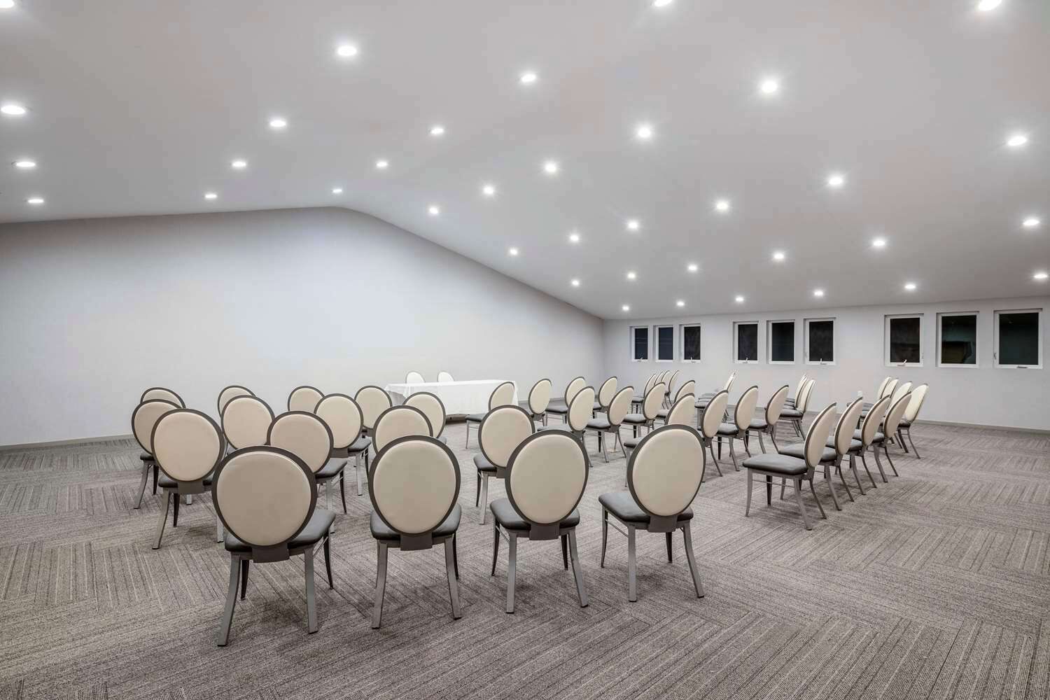 A large conference room with rows of chairs and tables, carpeted floor, and ceiling lights.