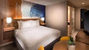 A hotel room with a large bed, two bedside tables with lamps, a round dining table with a potted plant, and a view of the hallway. - Aiden By Best Western Cape Cod - West Yarmouth (West Yarmouth)