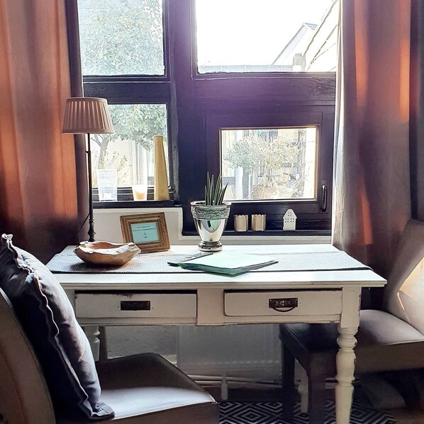 A room with a white desk, a lamp, a framed picture, and a view of trees through the window.