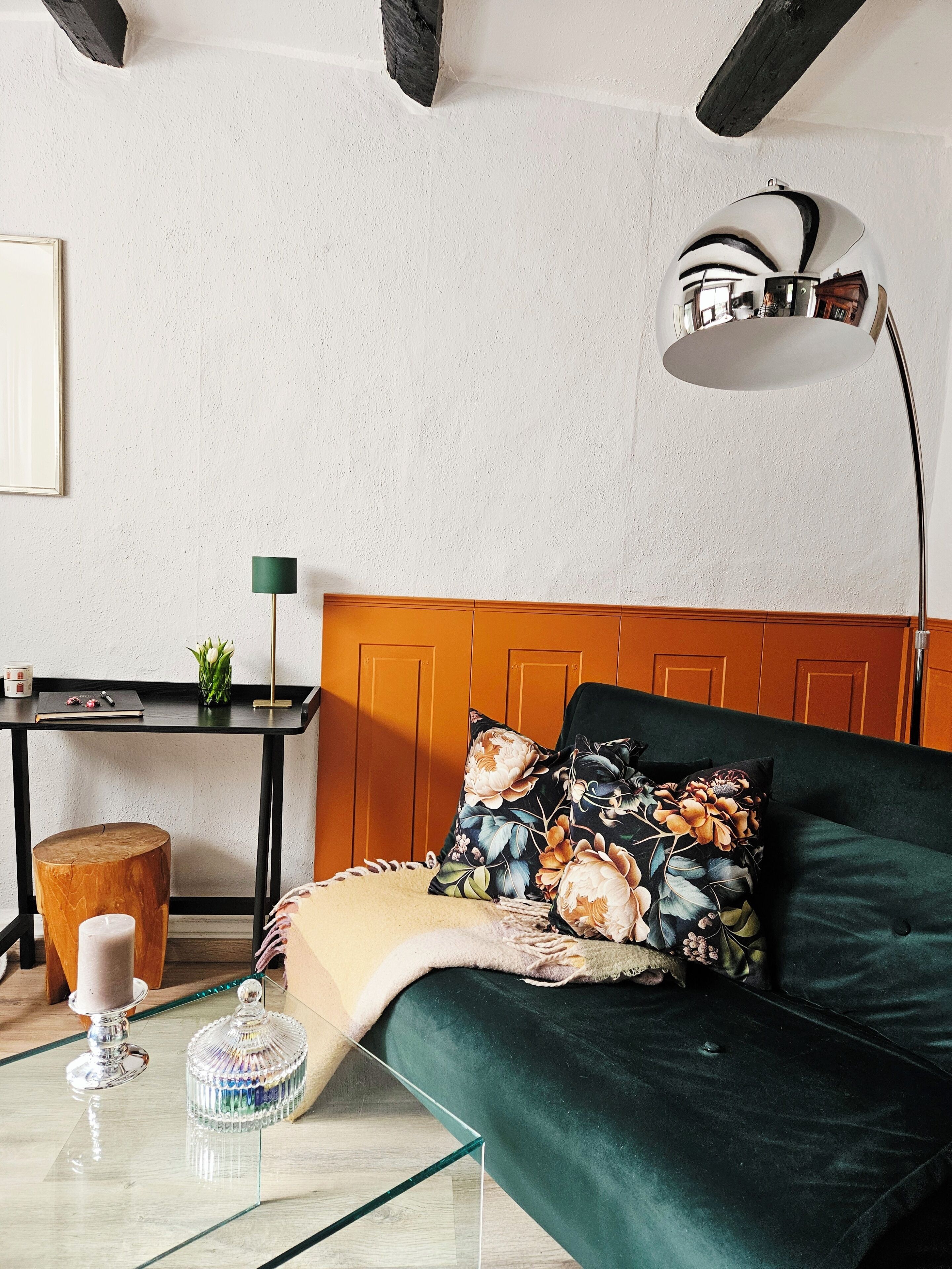 Ein Zimmer mit einem grünen Sofa, einem Holz-Bettgestell, einem Schreibtisch mit Lampe und einem kleinen Holzschemel.