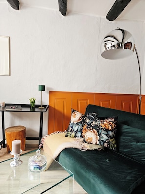 Una habitació amb un sofà verd, un panell de capçalera de fusta, un escriptori amb una làmpada i un petit tamboret de fusta.