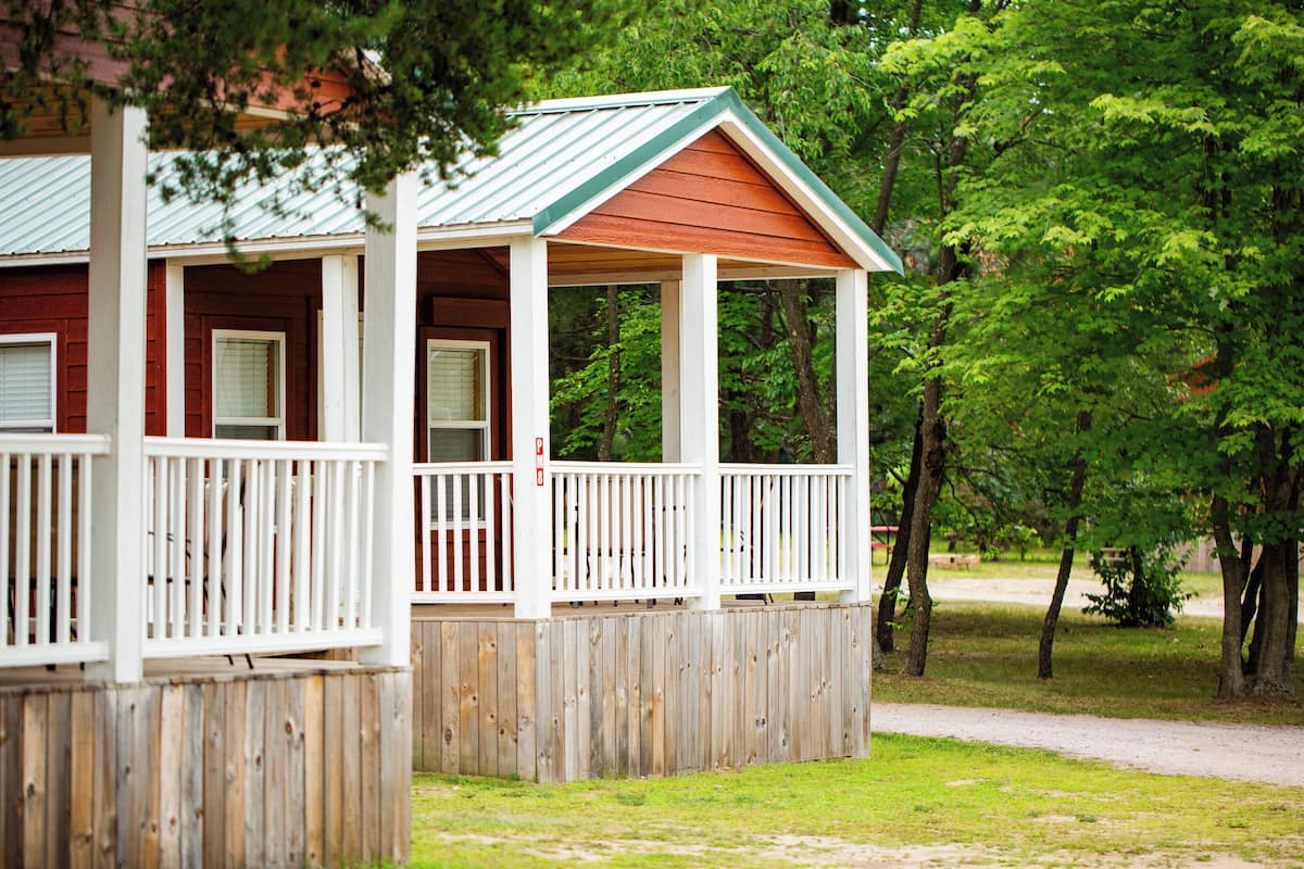 Une cabane en bois dotée d’un porche et d’un toit en métal, entourée d’arbres.