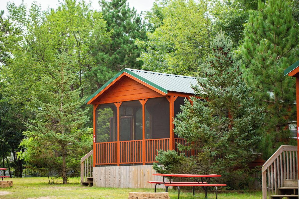 Une cabane avec une véranda et une table de pique-nique, située dans une zone boisée.