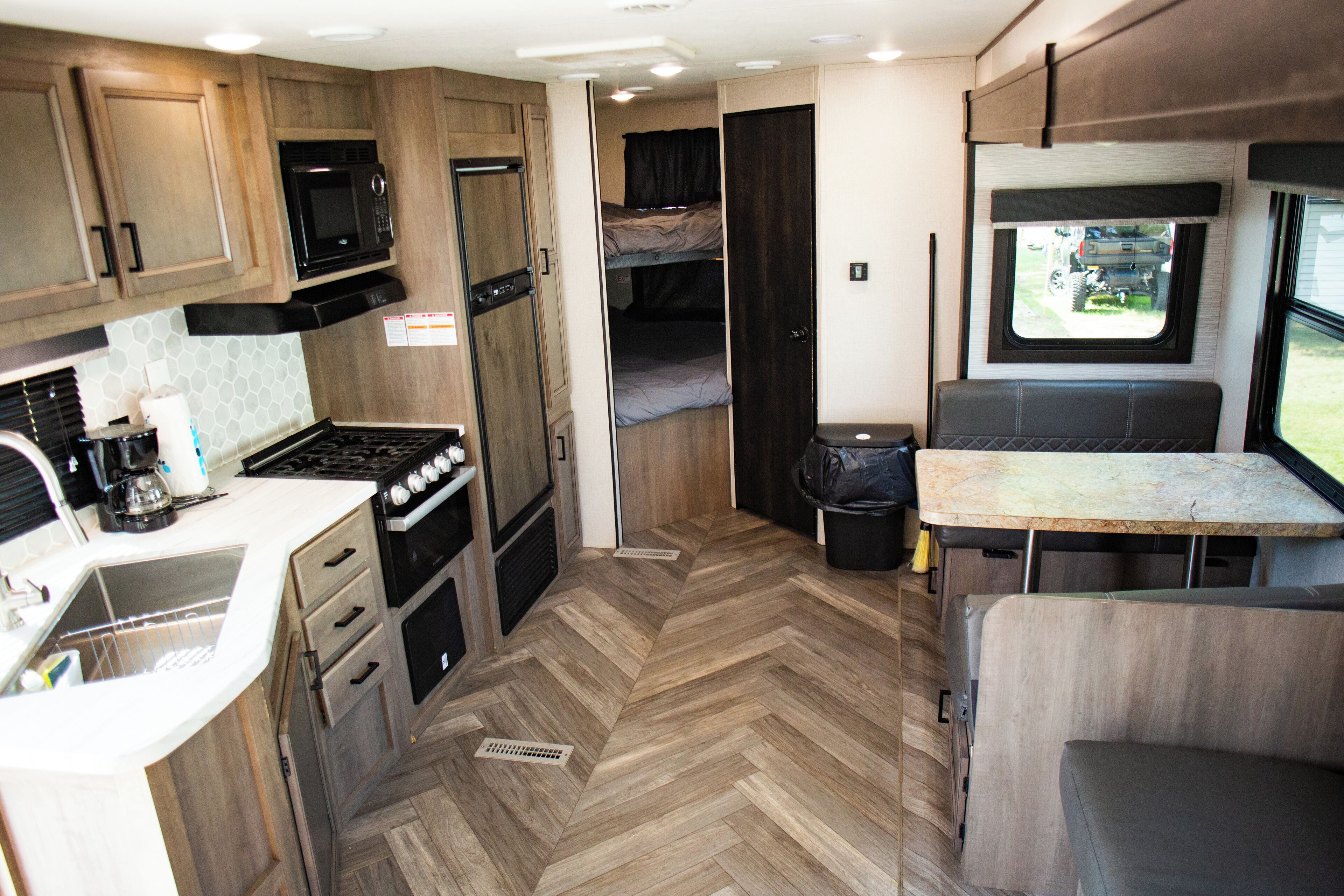 A compact RV kitchen with a microwave, stove, sink, and a small dining area.