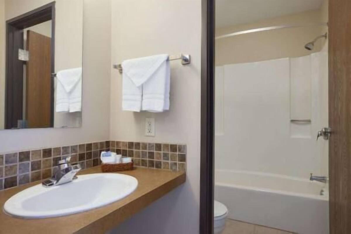 A bathroom with a sink, mirror, towel rack, shower, and toilet.