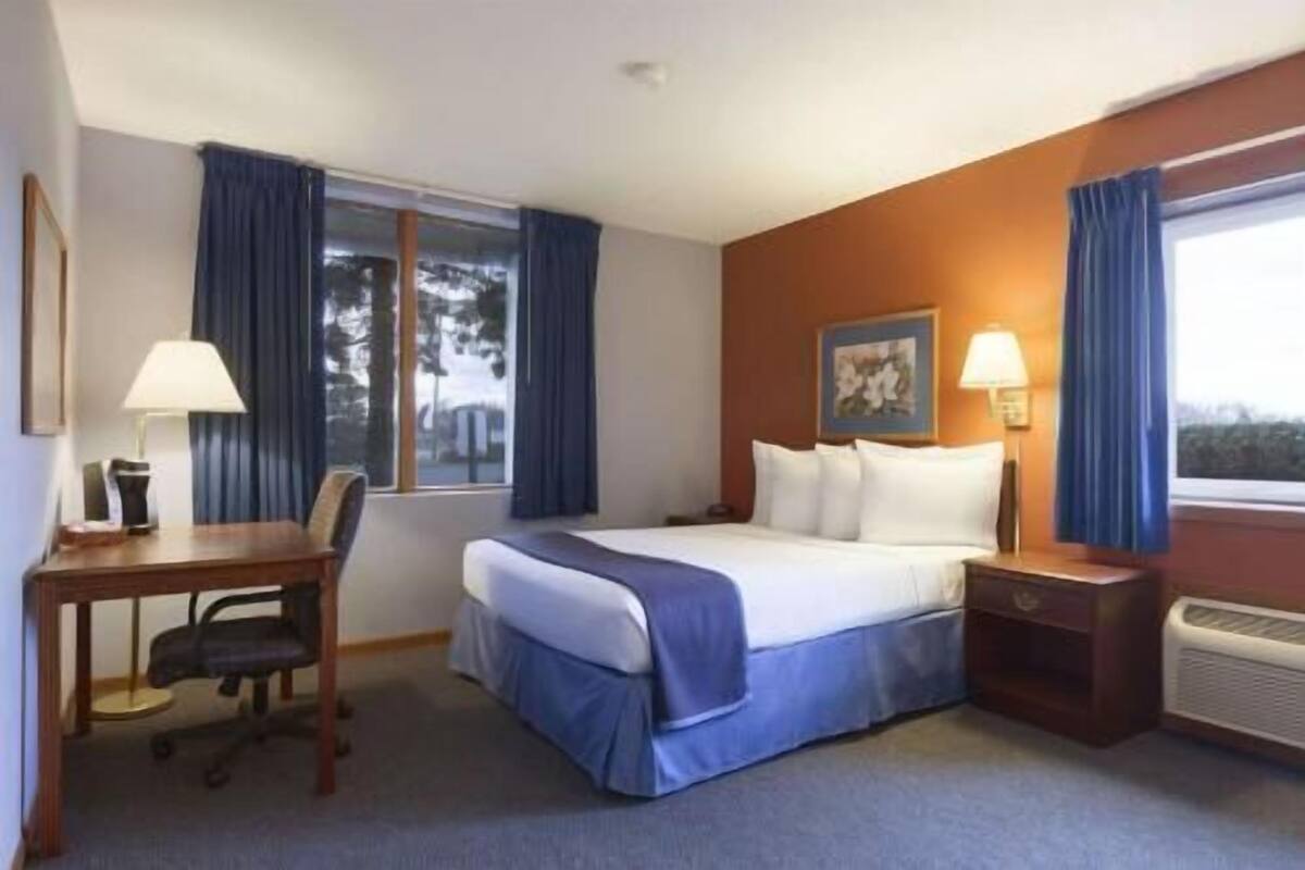 A hotel room with a bed, desk, chair, and a window with curtains.
