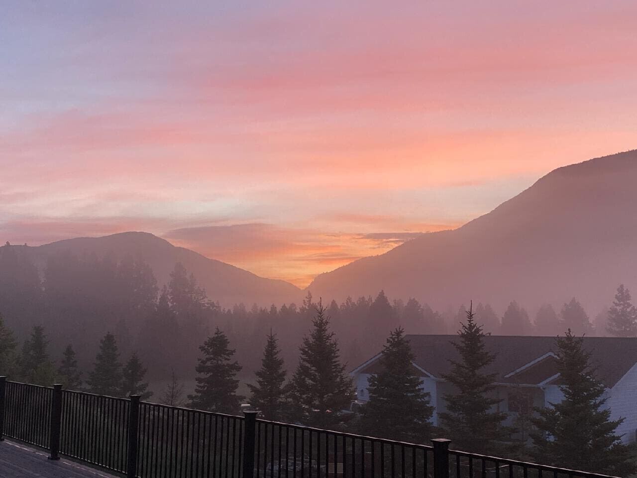 A mountain landscape with a sunset, houses, and a fence in the foreground.
