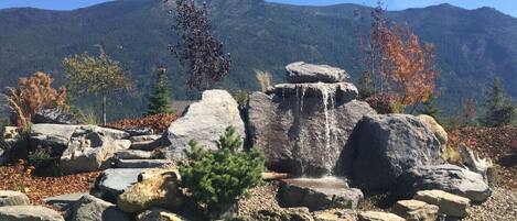 Formação rochosa natural com uma cascata, rodeada por folhagem outonal e montanhas ao fundo.