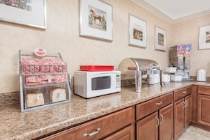 Una kitchenette equipada con microondas, tostadora y cafetera. En la pared hay cuadros enmarcados y un rack con pan y rollos de canela.