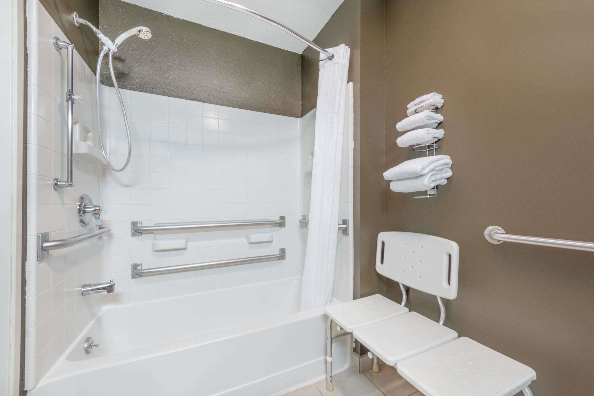 A bathroom with a walk-in shower, grab bars, a white bathtub, and a white bench.