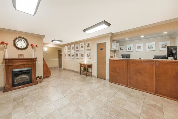 A reception area with a fireplace, a clock, framed pictures on the wall, and a reception desk. - Super 8 by Wyndham Georgetown (Georgetown)