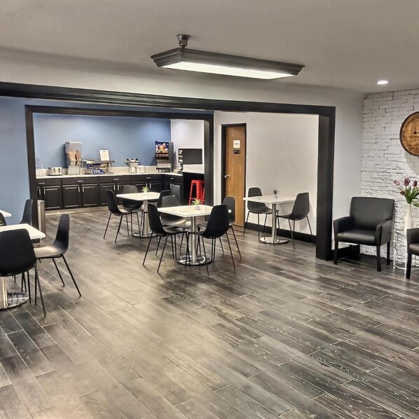 A modern dining area with tables and chairs, a kitchen in the background, and a brick wall. - Super 8 by Wyndham Georgetown (Georgetown)