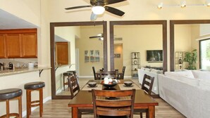 A dining area with a wooden table, chairs, and a ceiling fan. There is a kitchen area with wooden cabinets and a countertop. - Remodeled condo on PGA West's Stadium Golf Course (La Quinta)