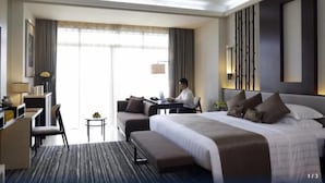 A hotel room with a large bed, a desk, a sofa, and a view of the outdoors. - Mission Hills Resort Haikou (Haikou)