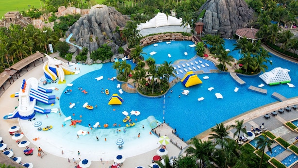A resort with a large central pool, multiple water slides, and a surrounding landscaped area with palm trees. - Mission Hills Resort Haikou (Haikou)