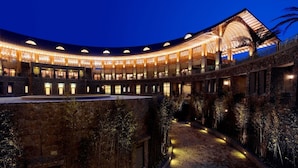 A large, multi-story building with a curved roof and multiple balconies, surrounded by stone walls and vegetation. - Mission Hills Resort Haikou (Haikou)