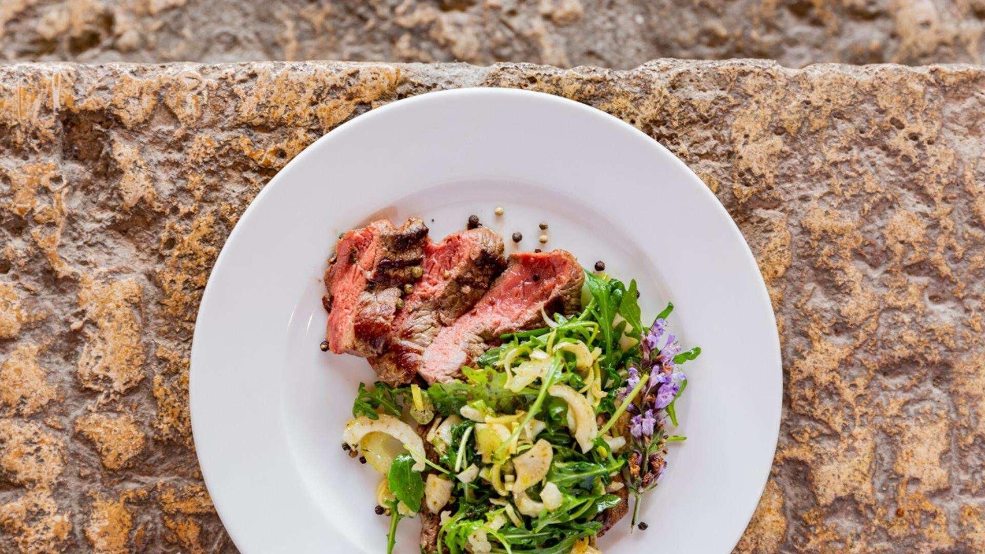 A plate of steak with a side salad on a granite countertop.