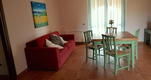 Un sofá rojo con almohadas, una mesa de comedor con sillas y un cuadro en la pared.
