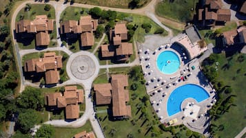 Vista aerea di una zona residenziale con diverse case, una strada ad anello e una piscina con lettini.
