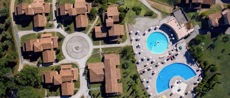 Vista aérea de una zona residencial con varias casas, un camino de entrada circular y una piscina con tumbonas.