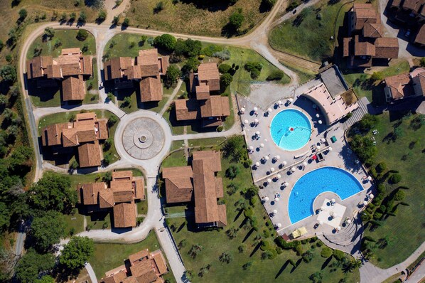 Vista aérea de una zona residencial con varias casas, un camino de entrada circular y una piscina con tumbonas.