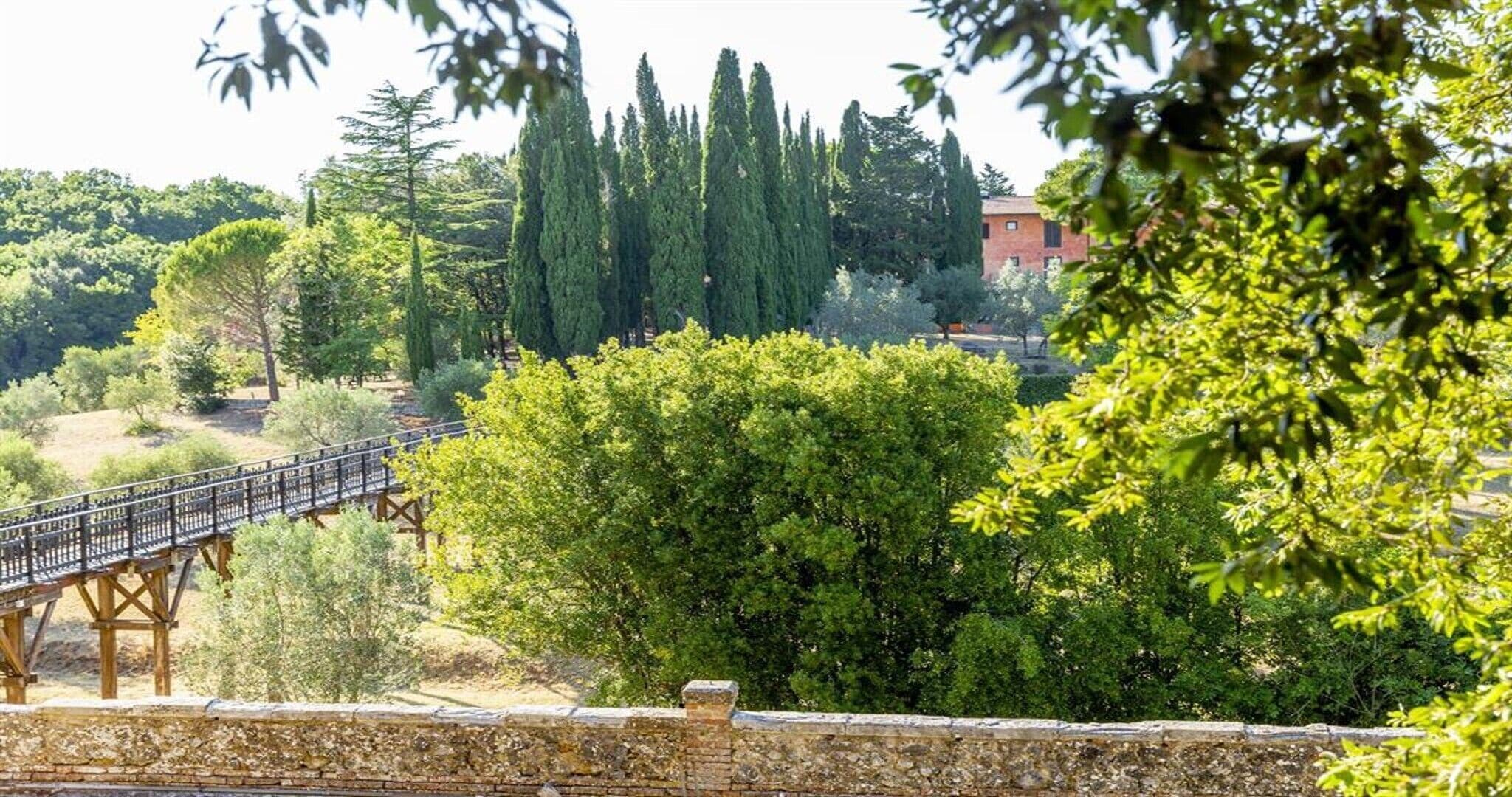 Un puente de piedra, abundante vegetación y un edificio al fondo.