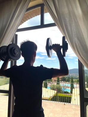 A person exercising with dumbbells near a window overlooking a pool and garden. - Pian Dei Mucini Resort (Massa Marittima)