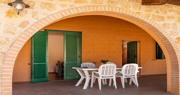 Un patio al aire libre con mesa y sillas, un arco y dos puertas abiertas.