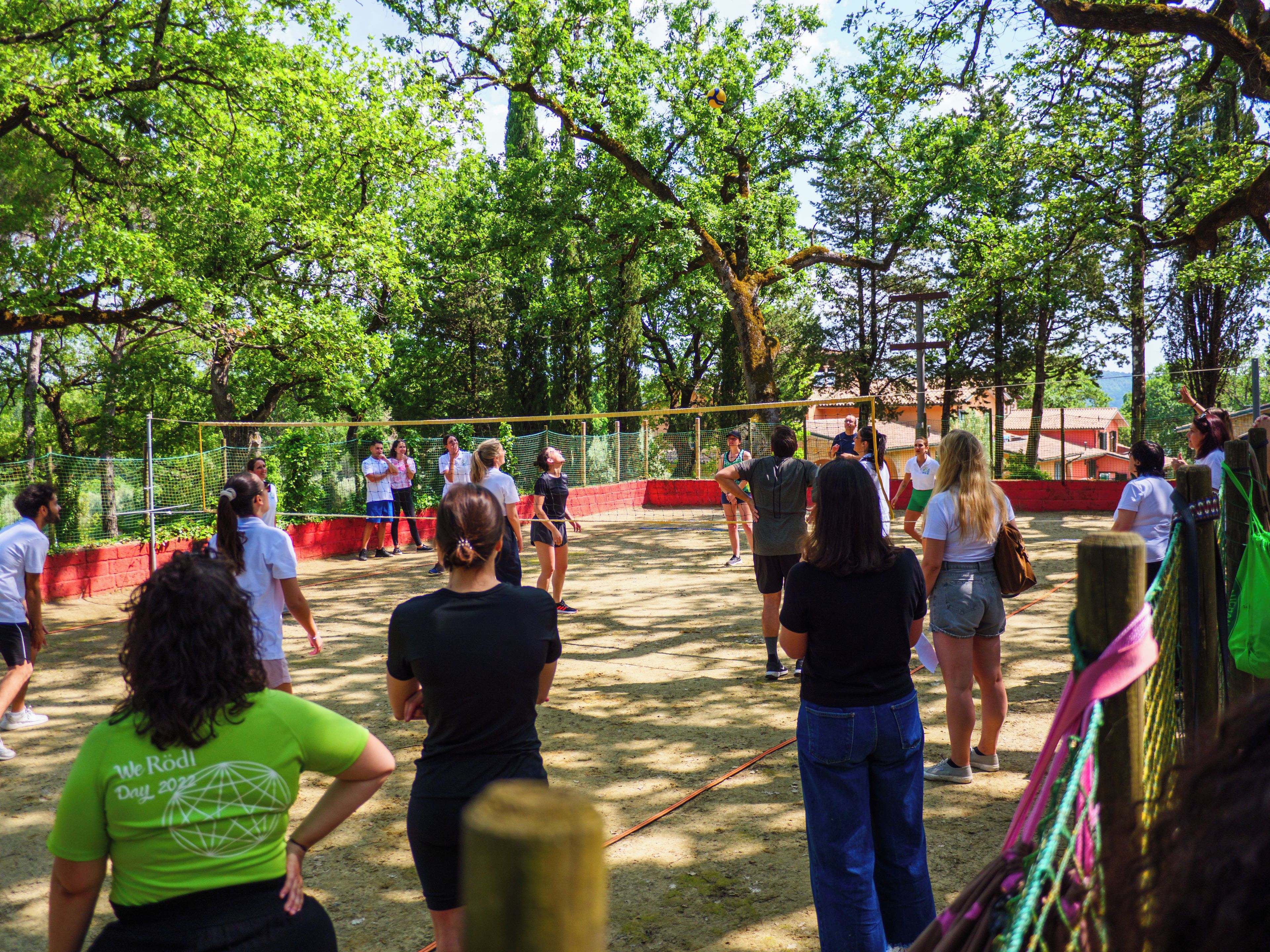 A group of people playing volleyball in an outdoor setting with trees and a net.