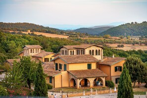 A large, multi-story building with a courtyard, surrounded by trees and hills. - Pian Dei Mucini Resort (Massa Marittima)