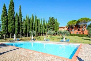 A swimming pool with lounge chairs and umbrellas, surrounded by tall trees and a building with a red facade. - Pian Dei Mucini Resort (Massa Marittima)