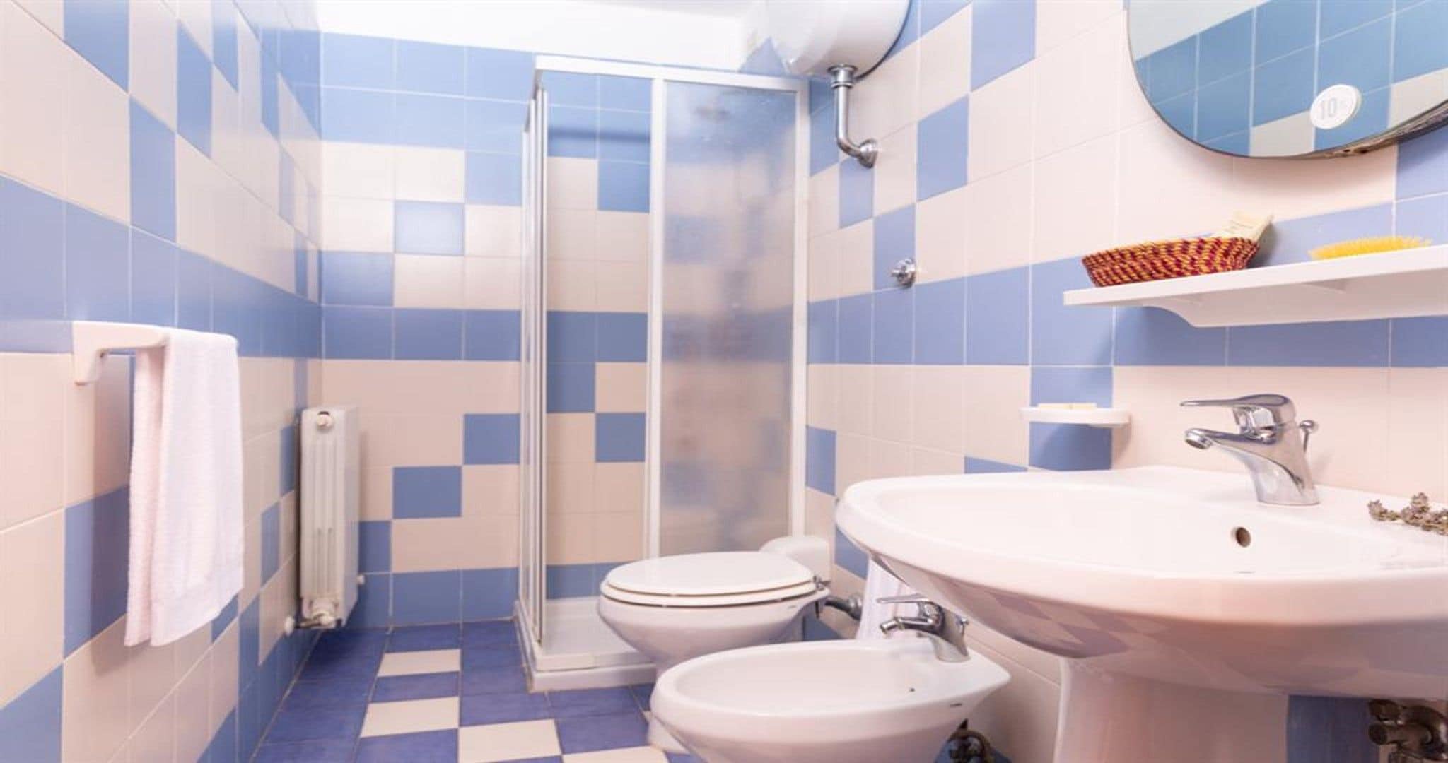 Un baño con ducha, inodoro y lavamanos, con azulejos blancos y azules a cuadros.