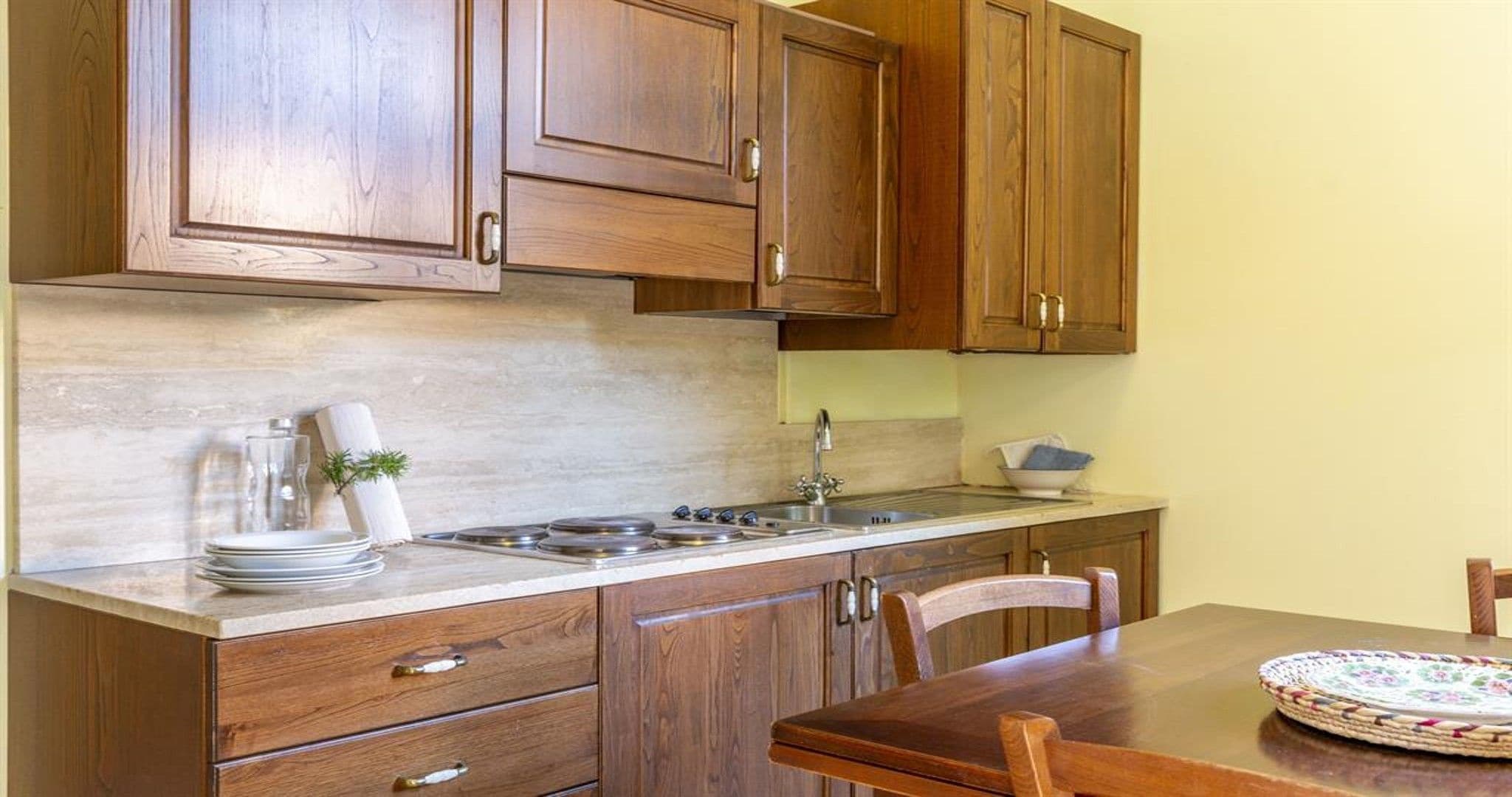 A kitchen with wooden cabinets, a stove, a sink, and a dining table with chairs.