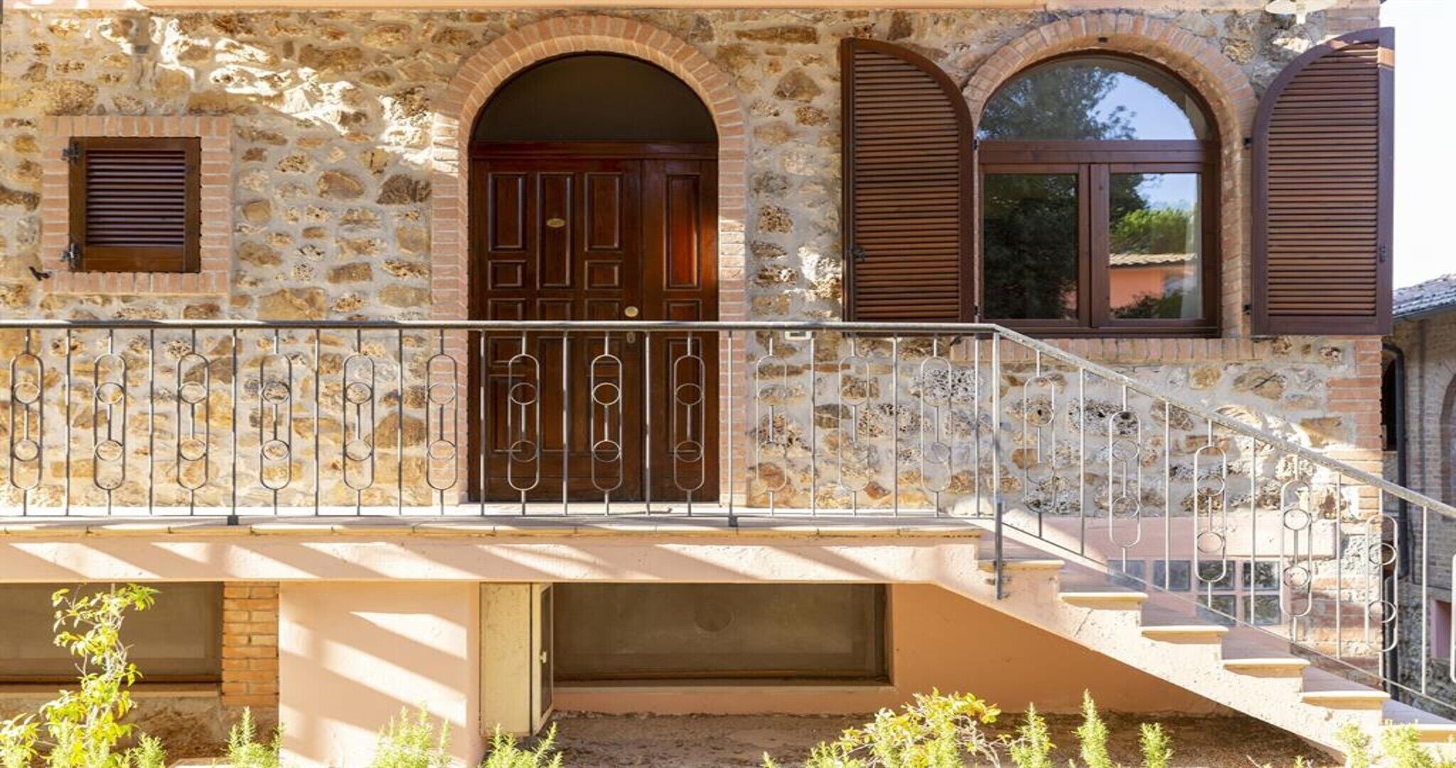 Un edificio de piedra con puerta de madera, una escalera y barandilla metálica.