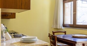 A kitchen with a wooden cabinet, a stove, and a dining table with chairs. - Pian Dei Mucini Resort (Massa Marittima)