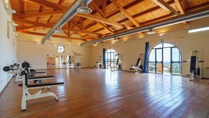 Un gimnasio amplio con vigas de madera, ventanas grandes y diversos equipos de ejercicio.