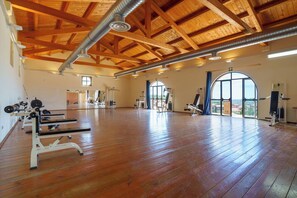 Un gimnasio amplio con vigas de madera, ventanas grandes y diversos equipos de ejercicio.