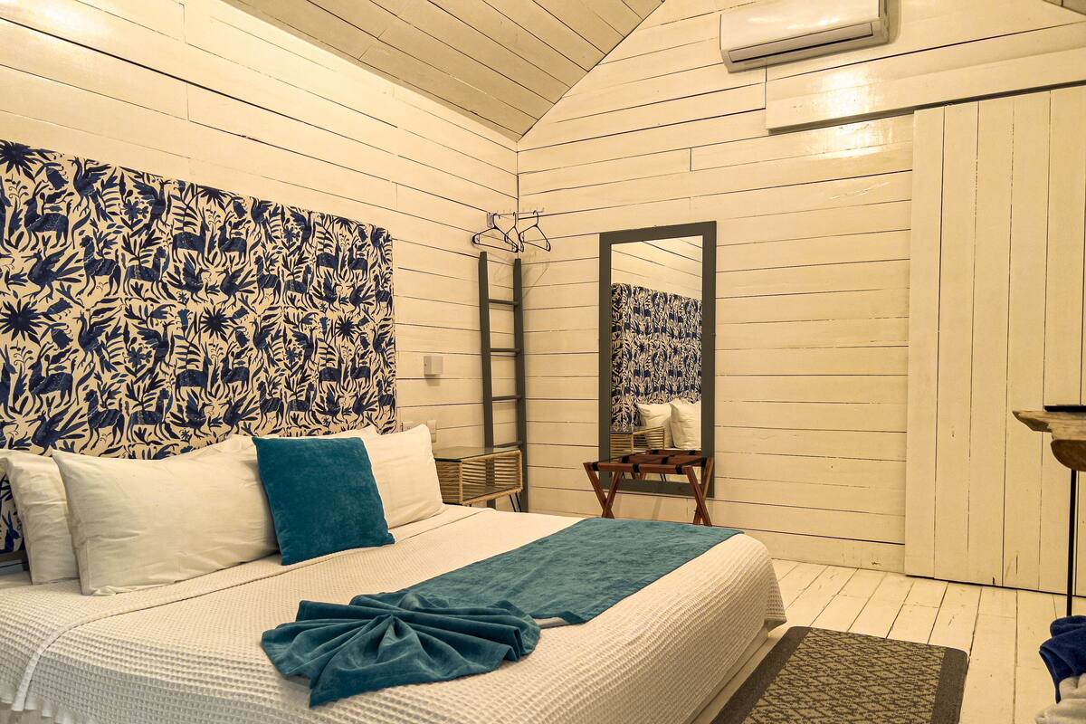 Un dormitorio con cama, espejo y ventana.