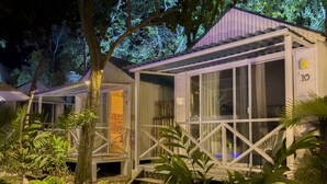 A row of small, white, single-story cabins with large windows, surrounded by lush greenery and trees. - Zensus Eco Boutique Hotel (Bacalar)