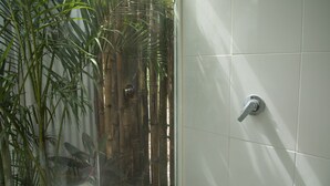 A bathroom with white tiled walls, a shower with a silver faucet, and a bamboo plant in the corner. - Zensus Eco Boutique Hotel (Bacalar)