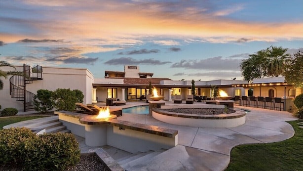 A modern outdoor pool area with fire pits, a staircase, and a covered seating area.