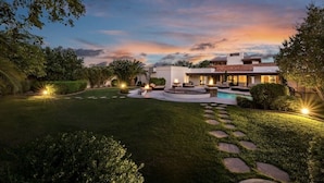 A modern house with a swimming pool, surrounded by well-maintained lawns and stone pathways.