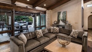 A modern living room with a sectional sofa, a coffee table, and a glass door leading to an outdoor patio area.
