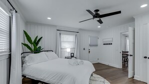 Une chambre avec un lit, un ventilateur de plafond, une plante en pot et une vue sur une autre pièce.