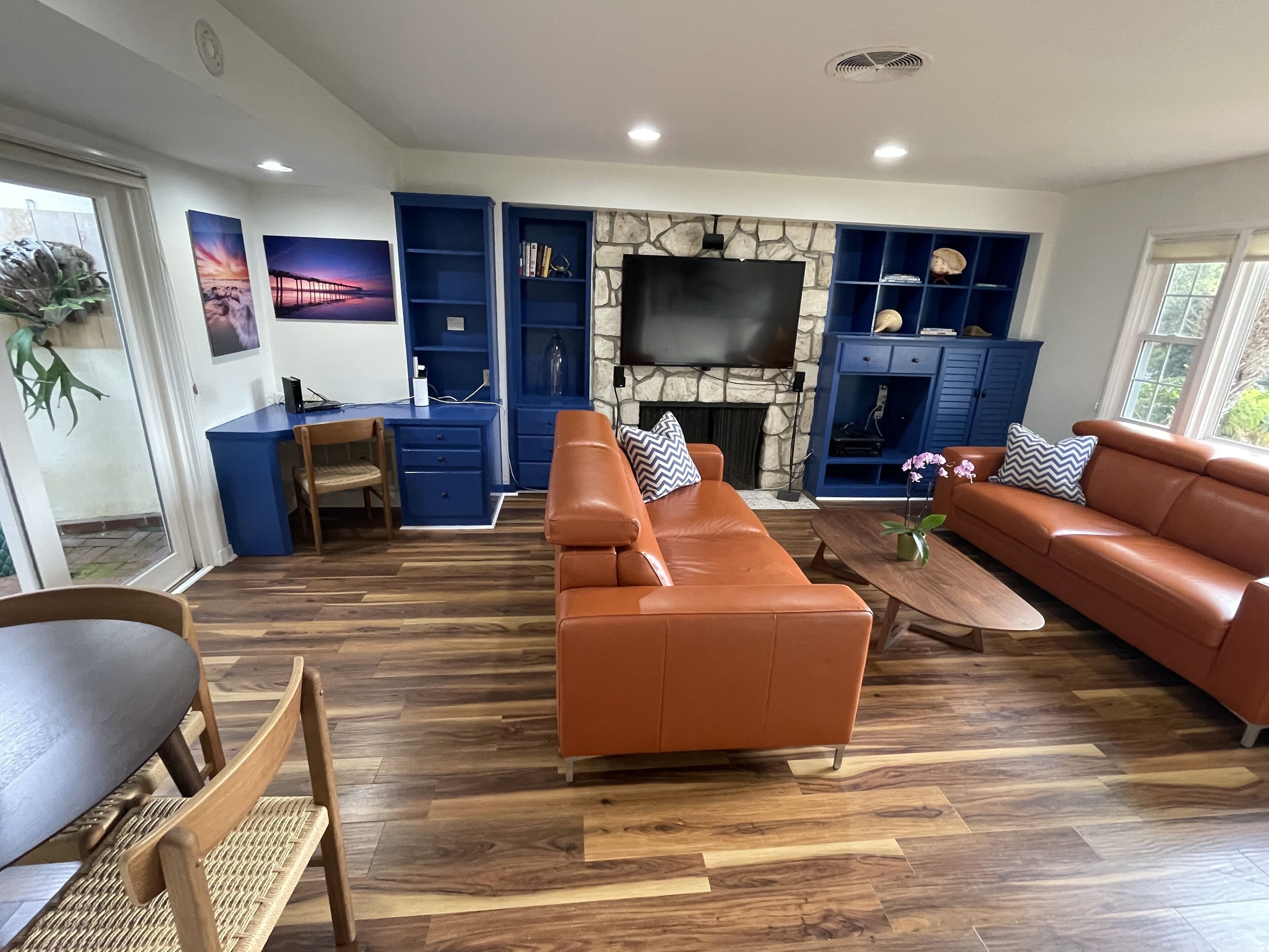 Una sala de estar moderna con chimenea de piedra, estanterías empotradas en azul, televisor de pantalla plana y sofás de cuero.