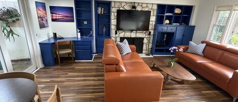 Una sala de estar moderna con chimenea de piedra, estanterías empotradas en azul, televisor de pantalla plana y sofás de cuero.