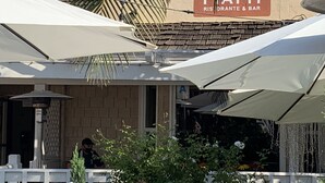 Ett utomhusområde med sittplatser och parasoller, en skylt med texten ”PIATTI RISTORANTE & BAR” och en person i bakgrunden.