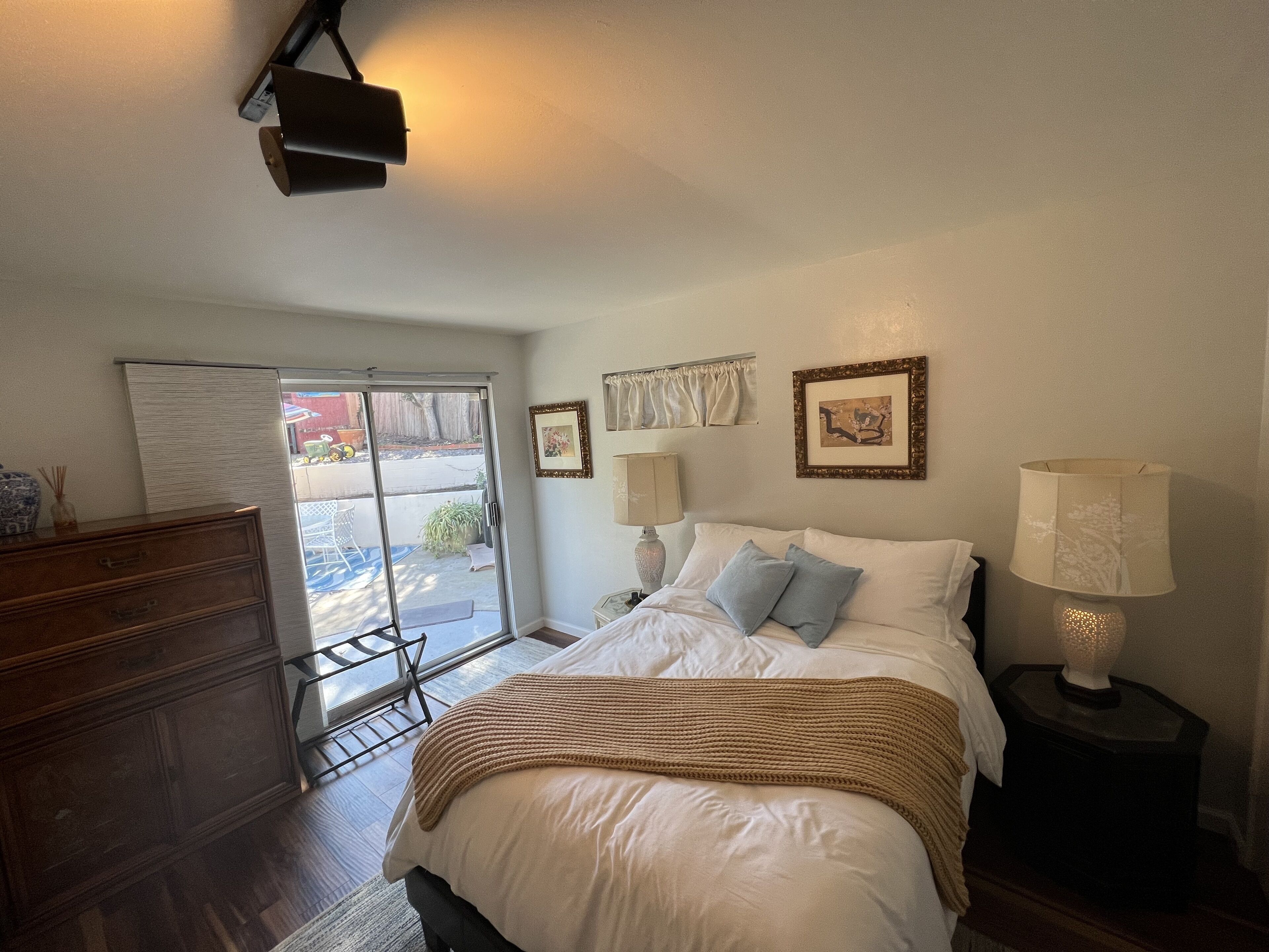 Un dormitorio con cama, lámparas de noche, cómoda y puerta corrediza de vidrio que da a un patio.