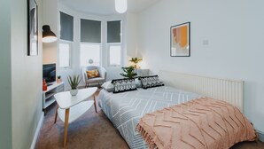 Een moderne, goed verlichte slaapkamer met een bed, nachtkastje en uitzicht op de stad door grote ramen.