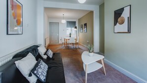 Een moderne woonkamer met een zwarte bank, witte kussens, een kleine witte tafel en een potplant.